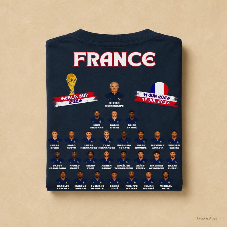 以下が含まれることがあります： 上部に「FRANCE」の文字、ワールドカップ2026のグラフィック、円形のフランス国旗がプリントされたダークネイビーのTシャツ。その下には、フランス代表サッカーチームの選手とディディエ・デシャン監督のポートレートと名前が記載されています。