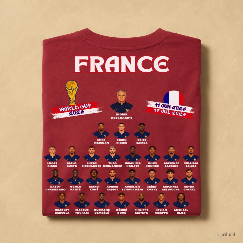 以下が含まれることがあります： 2026年ワールドカップに向けたフランス代表サッカーチームのメンバーがプリントされたカーディナルレッドのTシャツ。デザインには「FRANCE」の文字、ワールドカップトロフィー、2026年6月11日から7月19日までの日付、選手たちのポートレートが含まれています。