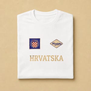 White unisex cotton T-shirt mockup with a clean Hrvatska football supporter graphic printed on the front. The design combines a small Croatian checkerboard-style shield, a vintage cream and blue Hrvatska patch, and bold neutral lettering underneath. The folded flat-lay image highlights the classic tee shape, soft cotton texture, balanced chest layout, and minimal national-pride design made for football season and general everyday wear.
