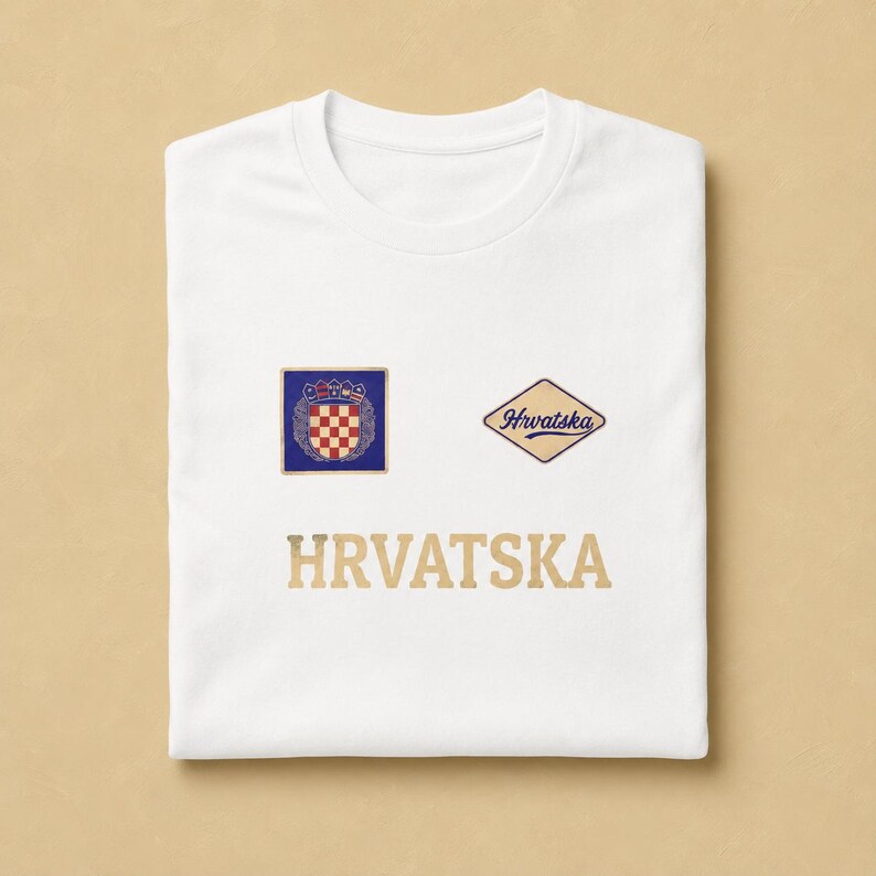 White unisex cotton T-shirt mockup with a clean Hrvatska football supporter graphic printed on the front. The design combines a small Croatian checkerboard-style shield, a vintage cream and blue Hrvatska patch, and bold neutral lettering underneath. The folded flat-lay image highlights the classic tee shape, soft cotton texture, balanced chest layout, and minimal national-pride design made for football season and general everyday wear.