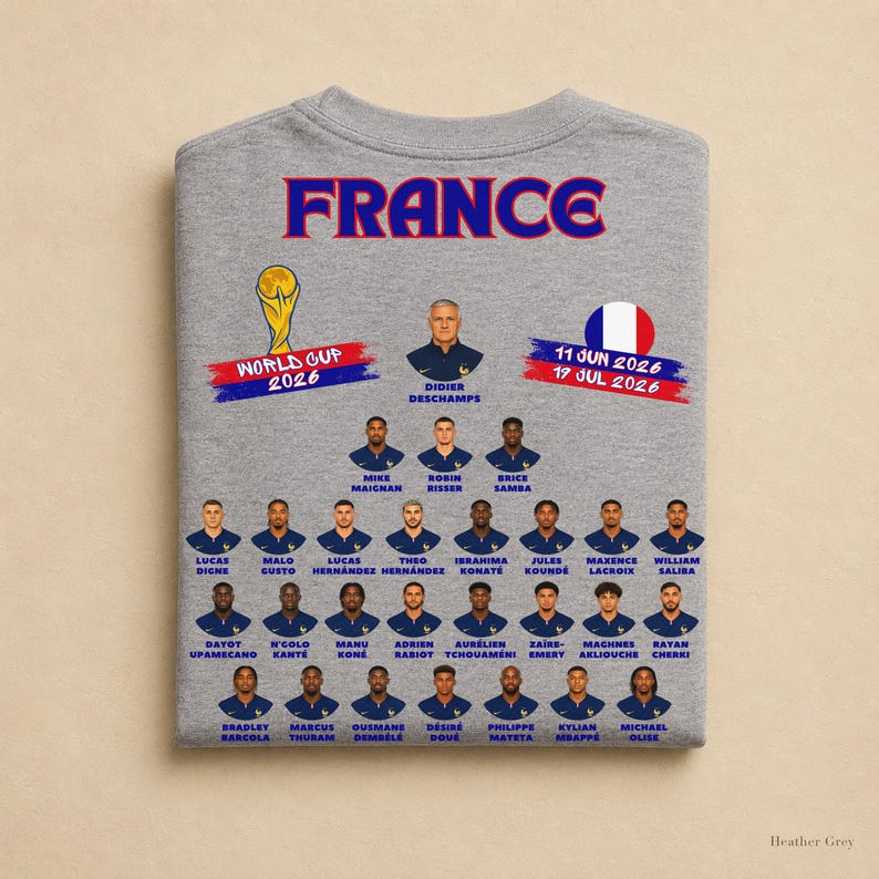 以下が含まれることがあります： 2026年ワールドカップに向けたフランス代表サッカーチームのメンバーがプリントされたヘザーグレーのTシャツ。デザインには「FRANCE」の文字、ワールドカップのトロフィー、フランス国旗、選手やスタッフのポートレートが含まれています。