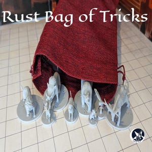 May include: A red fabric bag labeled "Rust Bag of Tricks" spills out several gray animal figurines on circular bases. The figurines include a boar, wolf, deer, and other creatures, suitable for tabletop gaming.