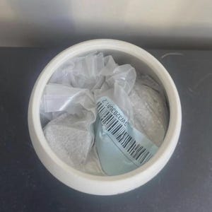 May include: A white ceramic bowl containing a clear plastic bag filled with a granular substance. A light blue adhesive label is attached to the plastic bag, featuring a black barcode and the printed alphanumeric text GW32035012.