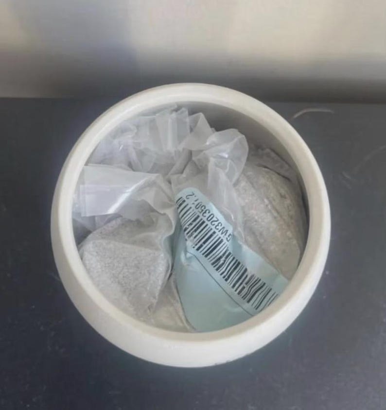 May include: A white ceramic bowl containing a clear plastic bag filled with a granular substance. A light blue adhesive label is attached to the plastic bag, featuring a black barcode and the printed alphanumeric text GW32035012.