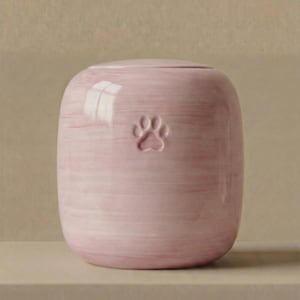 May include: A cylindrical ceramic urn with a soft pink, hand-painted finish featuring horizontal brushstroke textures. The front of the vessel displays a single, embossed paw print centered in the upper portion, topped with a matching rounded lid.