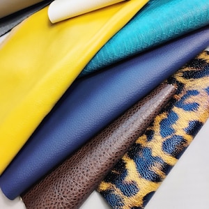 May include: A collection of colorful leather swatches in various textures. The colors include white, yellow, teal, navy blue, brown, and a leopard print. The leather appears to be smooth and textured, suitable for crafting or design projects.