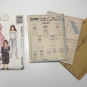 Può includere: Modelli di cucito vintage McCall's per abiti e tute. La busta del modello presenta illustrazioni dei capi finiti. Il numero del modello è 5340. Sono visibili ulteriori pezzi del modello.