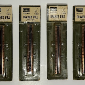 May include: Four Sears Craftsman antique copper drawer pulls in original packaging. Each package is labeled Drawer Pull, 3 inch centers, die-cast, and 60474. The pulls are long, rectangular, and metallic with a dark center and copper edges.