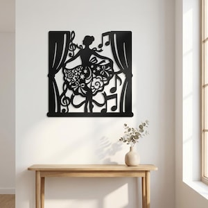 May include: Black metal wall art depicting a ballerina on a stage with musical notes and curtains. The ballerina is in a graceful pose, with a detailed floral skirt. The design is cut out, creating a silhouette effect.