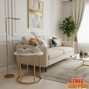 May include: A round side table with a white marble top and a gold metal frame, positioned next to a beige sofa. The table features a circular base and vertical support bars, providing a stable structure for the surface. The design is clean and simple.