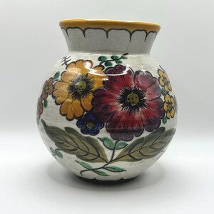 May include: A round ceramic vase with a cream-colored base featuring hand-painted floral motifs in shades of deep red, golden yellow, and green. The vase has a wide, scalloped rim with a yellow border and a glossy finish over the painted design.