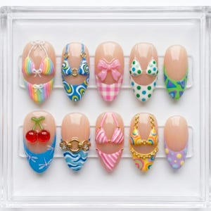 May include: A collection of ten artificial nails, each with a distinct design. The designs feature miniature bikini tops, cherries, and other summer-themed patterns. The nails are presented in a clear plastic case.