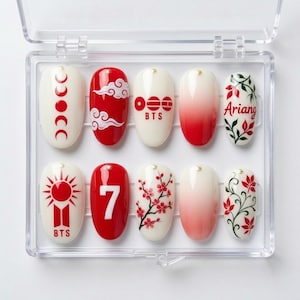 Könnte beinhalten: Ein Set aus zehn künstlichen Fingernägeln in einer transparenten Kunststoffbox. Die Designs umfassen rot-weiße Farbschemata, Mondphasen, Wolken, den Text BTS, die Zahl 7, Kirschblüten, rote Farbverläufe, grüne Ranken und das Wort Ariang.