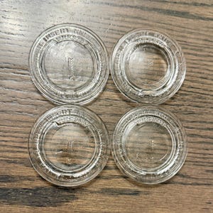 May include: Four circular, clear glass lids for canning jars. Each lid features embossed text reading "INSERT KNIFE AT NOTCH", "PRESTO", and "PAT RE 17562", along with a small arrow icon pointing toward a notch on the outer rim of the glass.