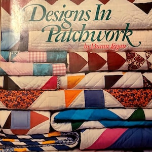 以下が含まれることがあります： Diann Logan著の書籍「Designs In Patchwork」の表紙。三角形、四角形、花柄など、様々な幾何学模様のカラフルなキルトが積み重なっている様子が描かれている。表紙には「30 Bright New Quilts for Machine Piecing」という文字が記されている。
