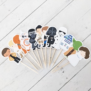 Puede incluir: Un conjunto de 12 adornos para cupcakes de personajes de Star Wars. Los adornos presentan personajes como Darth Vader, Yoda, la Princesa Leia, Chewbacca y R2-D2. Los adornos est&aacute;n impresos en cartulina y unidos a brochetas de madera.