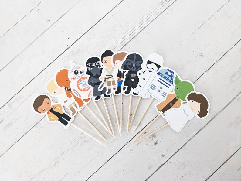 Puede incluir: Un conjunto de 12 adornos para cupcakes de personajes de Star Wars. Los adornos presentan personajes como Darth Vader, Yoda, la Princesa Leia, Chewbacca y R2-D2. Los adornos est&aacute;n impresos en cartulina y unidos a brochetas de madera.