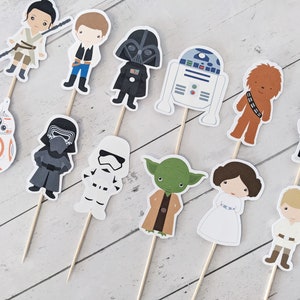 Puede incluir: Un conjunto de 12 adornos para cupcakes con tem&aacute;tica de Star Wars que presentan personajes como Darth Vader, Yoda, Chewbacca, la princesa Leia y R2-D2. Los adornos est&aacute;n impresos en cartulina y unidos a brochetas de madera.