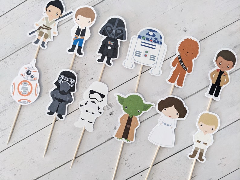 Puede incluir: Un conjunto de 12 adornos para cupcakes con tem&aacute;tica de Star Wars que presentan personajes como Darth Vader, Yoda, Chewbacca, la princesa Leia y R2-D2. Los adornos est&aacute;n impresos en cartulina y unidos a brochetas de madera.