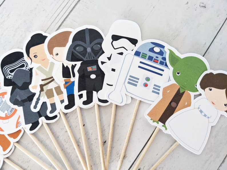 Puede incluir: Un conjunto de 12 adornos para cupcakes de personajes de Star Wars. Los adornos presentan personajes como Darth Vader, Yoda, R2-D2 y la princesa Leia. Los adornos est&aacute;n impresos en cartulina y unidos a brochetas de madera.