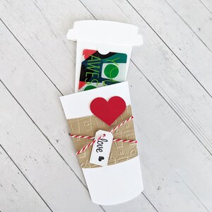 Puede incluir: Un vaso de caf&eacute; de papel blanco con una tarjeta de regalo dentro. El vaso est&aacute; decorado con un coraz&oacute;n rojo y una etiqueta que dice "love".