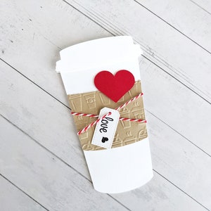 Puede incluir: Un vaso de caf&eacute; de papel blanco con un coraz&oacute;n rojo y una etiqueta de papel marr&oacute;n que dice "love".