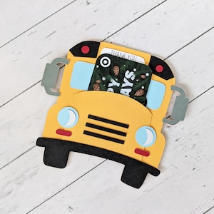 May include: A yellow school bus-shaped card holder with black wheels and accents. The bus has blue windows, red lights, and grey side mirrors. A card with a pine cone design and the words "THANK YOU" and "HAPPY DAYS" is inserted into the holder.