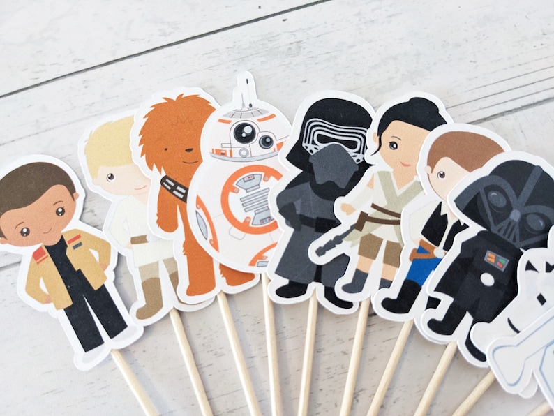 Puede incluir: Un conjunto de 10 adornos para cupcakes de personajes de Star Wars. Los adornos presentan personajes como Darth Vader, Chewbacca, Rey y Finn. Los adornos est&aacute;n impresos en cartulina blanca y unidos a brochetas de madera.