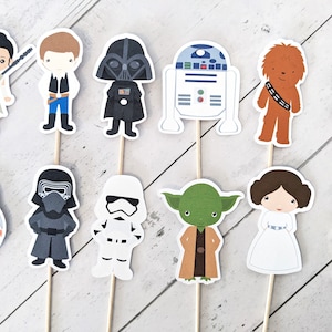 Puede incluir: Conjunto de 10 adornos para cupcakes de personajes de Star Wars. Los adornos presentan personajes como Darth Vader, Chewbacca, R2-D2, Yoda y la Princesa Leia. Los adornos est&aacute;n impresos en cartulina y unidos a palos de madera.