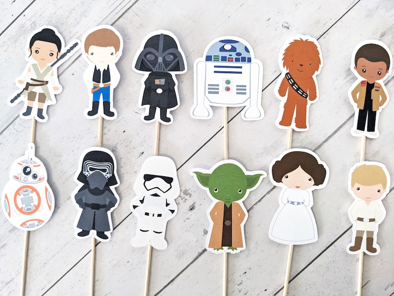 Puede incluir: Conjunto de 10 adornos para cupcakes de personajes de Star Wars. Los adornos presentan personajes como Darth Vader, Chewbacca, R2-D2, Yoda y la Princesa Leia. Los adornos est&aacute;n impresos en cartulina y unidos a palos de madera.