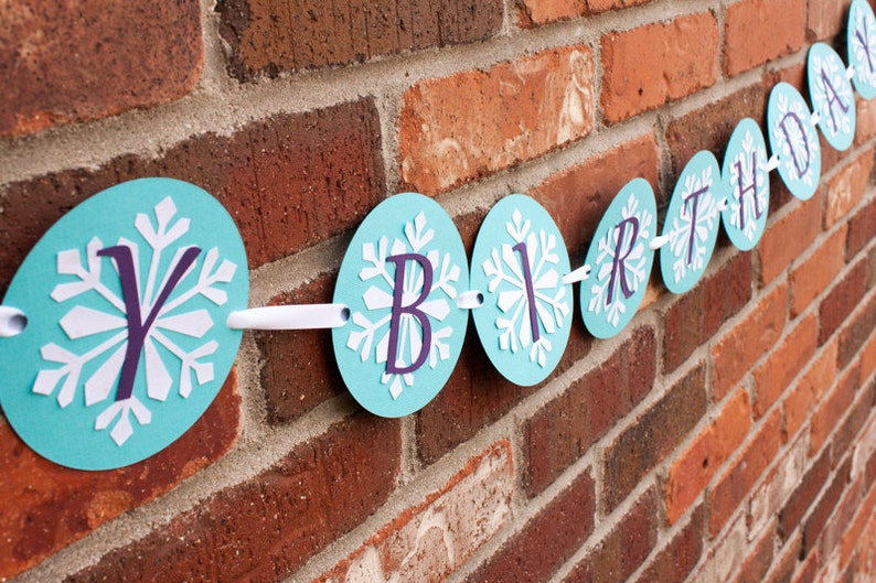 K&ouml;nnte beinhalten: Ein blaues und wei&szlig;es Geburtstagsbanner mit Schneeflockenmustern und dem Wort "Birthday" in lila Buchstaben.