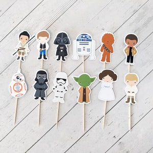 Puede incluir: Conjunto de 12 adornos para tartas de personajes de Star Wars. Los adornos representan personajes como Darth Vader, Yoda, la princesa Leia, Chewbacca y R2-D2. Los adornos est&aacute;n impresos en cartulina y unidos a brochetas de madera.