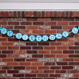 K&ouml;nnte beinhalten: Ein blaues und wei&szlig;es Banner mit den Worten "Happy Birthday Lily" an einer Backsteinmauer.