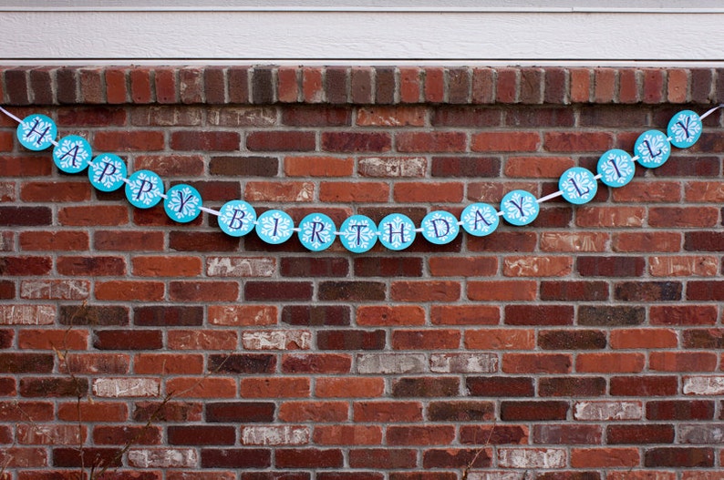 K&ouml;nnte beinhalten: Ein blaues und wei&szlig;es Banner mit den Worten "Happy Birthday Lily" an einer Backsteinmauer.