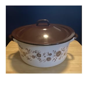 May include: A white enamel pot with a dark brown lid and matching brown floral pattern around the exterior. The pot features two side handles and a central handle on the lid. The finish is glossy, and the design consists of repeating brown flowers.