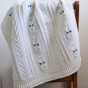 May include: White crocheted baby blanket with a cable knit pattern and blue owl appliques.