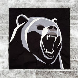 May include: Black and white geometric illustration of a bear with its mouth open, showing its teeth. The bear is facing the right side of the image.