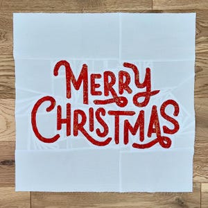 Könnte beinhalten: Weißer Stoff mit einer roten "Frohe Weihnachten"-Botschaft in einer stilisierten Schrift.