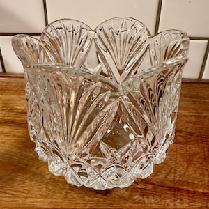 May include: A clear glass bowl featuring a scalloped rim with a fan-like pattern and a diamond-cut texture on the lower body. The vessel has a wide opening and a rounded base, reflecting light through its faceted surfaces and intricate pressed glass design.