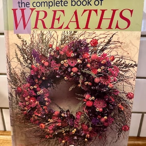 May include: A hardcover book titled the complete book of WREATHS with 200 delightful & creative designs. The cover features a large, circular wreath made of dried twigs, purple, pink, and red flowers, set against a light, neutral background.