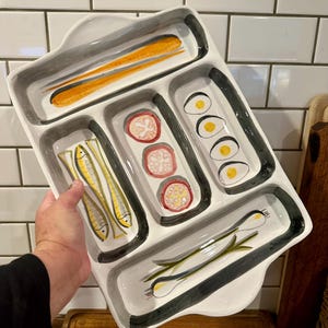 May include: A white ceramic serving tray with five distinct compartments, each featuring hand-painted illustrations. The designs include yellow fish, orange carrots, pink circular slices, yellow-centered eggs, and green scallions, all outlined in gray.