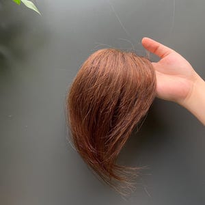Op de afbeelding: Een haartopper met steile, halflange lokken in een warme auburnbruine tint. Het haar is gestyled met een natuurlijke, gelaagde textuur en een gladde afwerking, ontworpen om volume en dekking te bieden voor de bovenkant van het hoofd.