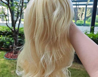 Peut inclure: Une perruque longue et ondulée aux cheveux blond clair avec de subtils reflets platine. Les cheveux présentent une texture volumineuse et dégradée avec des boucles douces tombant sur toute la longueur, offrant un aspect naturel et nuancé.