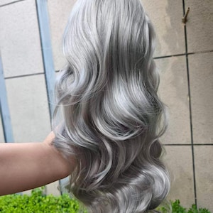 May include: A long, wavy wig featuring a metallic silver and platinum gray color palette. The hair is styled with voluminous, cascading curls that flow downward, showcasing a smooth, glossy texture and multi-tonal highlights throughout the strands.