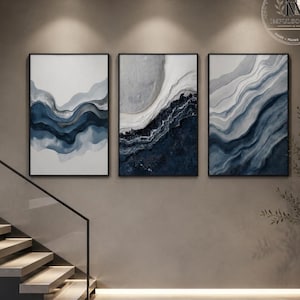 Puede incluir: Un conjunto de tres láminas de arte mural rectangulares con diseños abstractos fluidos en tonos azul marino, gris pizarra y blanco. Cada pieza está enmarcada en un marco negro fino, mostrando patrones ondulados superpuestos que imitan texturas.