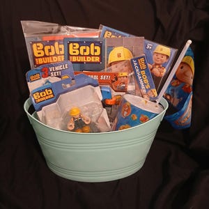Peut inclure: Un seau en métal vert menthe clair rempli d'articles sur le thème de Bob le Bricoleur, incluant un ensemble de 3 véhicules, un jouet marteau-piqueur, une figurine de Bob, un gobelet avec paille et diverses cartes emballées montrant le personnage.
