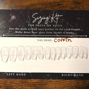 Op de afbeelding: Een rechthoekige maattabelkaart voor plaknagels met een zwart marmeren bovengedeelte en een wit ondergedeelte. De tekst luidt Sizing Kit, For Press-on Nails, Use the nails to find your perfect fit for each finger, Write down your sizes from thumb to pinky, Nail Shape: Coffin, Left Hand en Right Hand. Een rij doorzichtige, doodskistvormige nageltips is in het midden bevestigd.