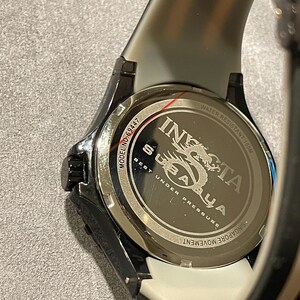 May include: The back of an Invicta Subaqua watch with a black case and a two-tone strap. The stainless steel case back features the text Invicta, Subaqua, Model No. 69447, Water Resistant 100M, Best Under Pressure, and Singapore Movement.