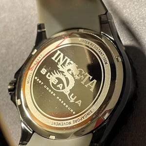 May include: The stainless steel case back of an Invicta Subaqua watch features the text INVICTA SUBAQUA, BEST UNDER PRESSURE, WATER RESISTANT 100M, MODEL NO 69447, and SINGAPORE MOVEMENT. A dragon graphic is engraved in the center of the metallic surface.