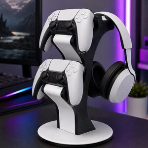 May include: A black and white gaming accessory stand featuring a circular base and a vertical support structure. The stand holds two white and black wireless game controllers stacked vertically and a pair of white over-ear headphones on the side.